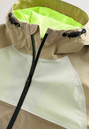 Bež in svetlo zelena jakna z mrežno teksturo, visokim ovratnikom, zadrgo, nastavljivo kapuco in zračno notranjo oblogo.