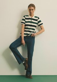 Pasiasty polo w kolorze zielonym i białym, z krótkim zamkiem i kołnierzykiem. Połączony z ciemnoniebieskimi spodniami dzwonami i czarnymi butami na platformie.