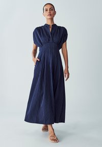 Navy striped maxi dress with a high collar, puffed short sleeves, and a fitted waist, featuring side pockets and a flowing skirt.