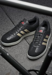 Czarne sneakersy wykonane z syntetycznej skóry z złotymi paskami, teksturowanymi akcentami, perforacjami oraz białą gumową podeszwą. Czerwone logo na języku.