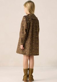 Robe marron à motifs avec col à volants, manches longues et taille cintrée, associée à des bottines marron. Vue de dos montrant une jupe évasée.