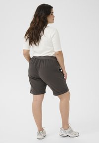 Hnědé culotte šortky s ohrnutými manžetami, elastickým pasem a bočními kapsami, v kombinaci s fitted bílým topem a bílými sportovními botami.
