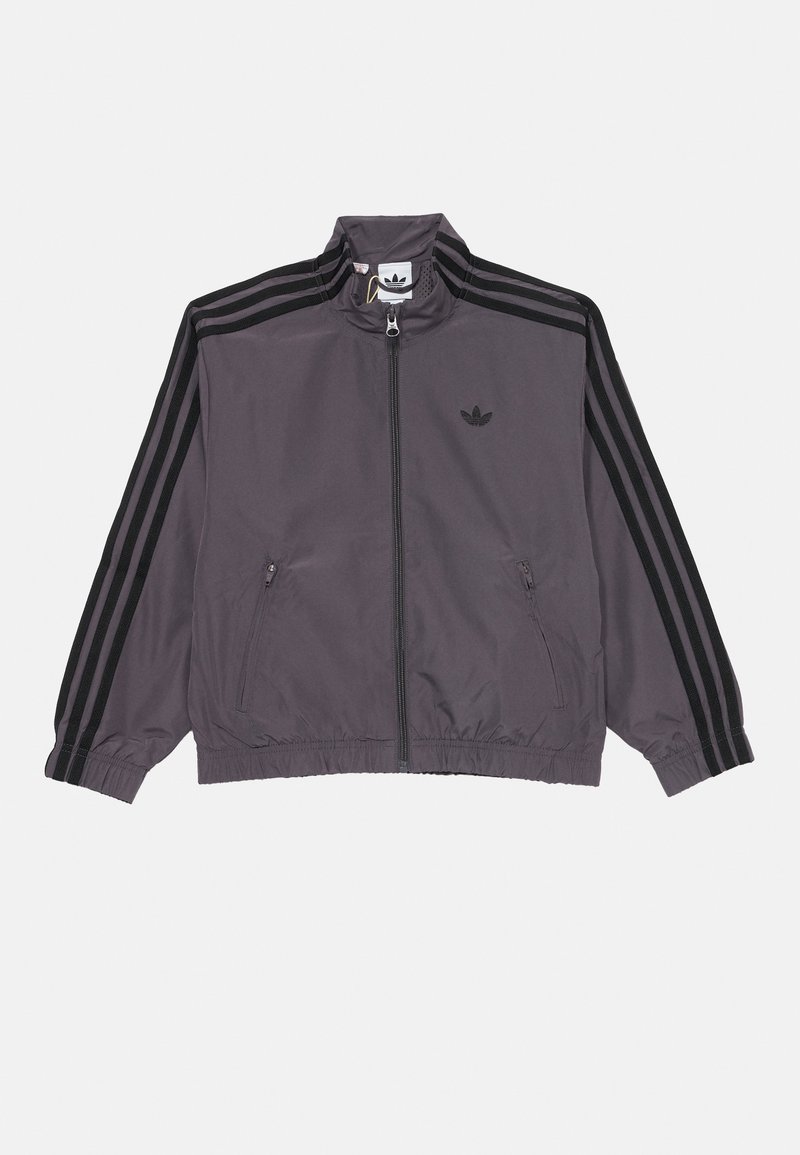 Zadrževalna jakna v temno sivi barvi, s črnimi črtami po rokavih in vezenim logotipom na prsih. Lahka, elastična manšeta in rob.