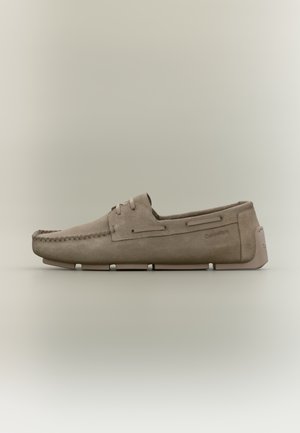 Bēša zamšādas mokasīns ar moc toe šuvēm, mežģīņu detaļu, šķeltu zoli un Calvin Klein logotipu pusē un papēža cilpā.