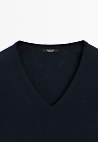 Maglione blu navy a V con una texture liscia, con l'etichetta "Massimo Dutti" visibile sul colletto, posto su uno sfondo semplice.