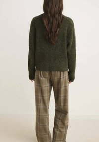 Pulover texturat, de culoare verde închis, cu mâneci lungi, asortat cu pantaloni bej în carouri cu linii albastre, pentru un aspect elegant.
