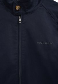 Navyblå jakke med lynlåslukning og knapper, med "POLO CLUB" broderet på brystet og lynlåstrækket.