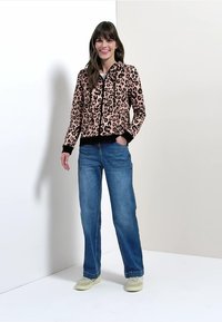 Leopardprint lynlåstrøje med sorte detaljer og ribstrikkede manchetter, stylet med blå jeans med lige ben og lyse sneakers.