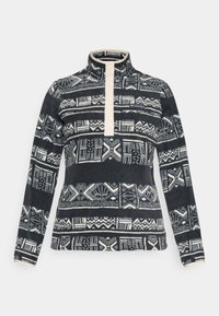 Fleece genser med høy krage, med en kremfarget knappeåpning og svart-hvite abstrakte geometriske mønstre over hele.