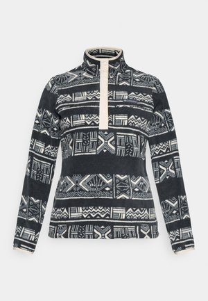 Pull en polaire avec un col haut, présentant une patte de boutonnage crème et des motifs géométriques abstraits noirs et blancs sur toute la surface.