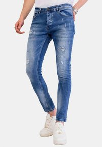 Strakke blauwe denim jeans met slijtage, verfspatten en een vijf-vakken ontwerp. Voorzien van een knoopsluiting en riemlussen.