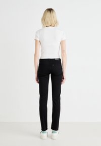 Svarta slim-fit jeans med medelhög midja, bakfickor och subtila sömnadsdetaljer, kombinerat med en figurnära vit t-shirt och vita sneakers.