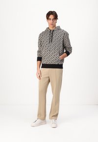 Hooded sweatshirt in black and white patterned fabric, with a drawstring, elastic cuffs, and hem. Paired with light beige trousers and white shoes.