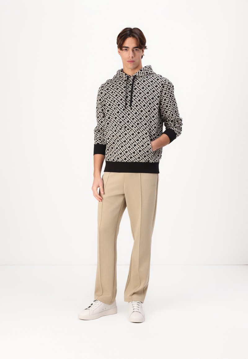 Felpa con cappuccio in tessuto stampato bianco e nero, dotata di un cordino, polsini elasticizzati e orlo. Abbinata a pantaloni beige chiaro e scarpe bianche.