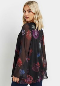 Kimono nero trasparente con motivo floreale multicolore, maniche fluttuanti, orlo scalloppato e una texture leggera. Adatto per il layering.