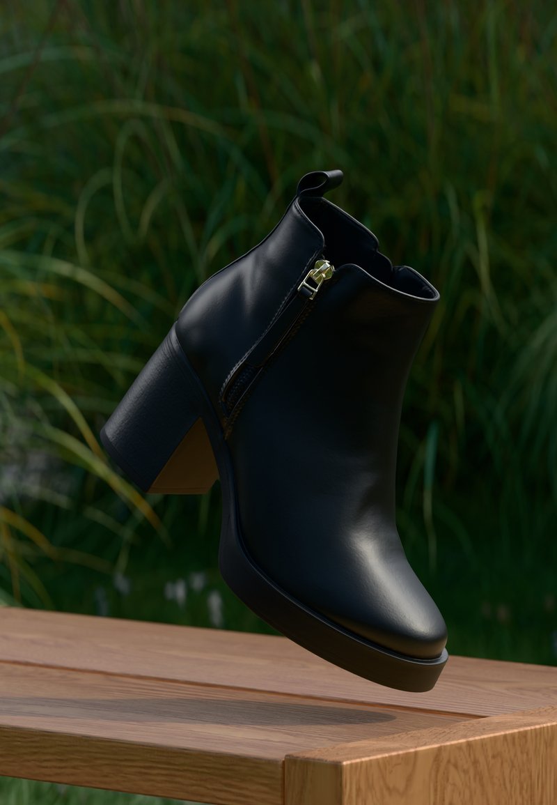 Crna kožna gležnjača s izraženom petom, bočnim zatvaračem i glatkom teksturom, prikazana na drvenoj površini uz zelenu pozadinu.