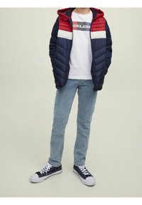 Marinhalsfarvad och röd vadderad pjakke med huva, vit panel; kombinerad med vit grafisk t-shirt, ljusblå jeans och marinblå sneakers.