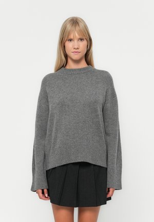 Grå strikkegenser med rund hals og ribbestrikkede mansjetter, kombinert med et svart plissert skjørt. Myk tekstur, avslappet passform og uformell design.