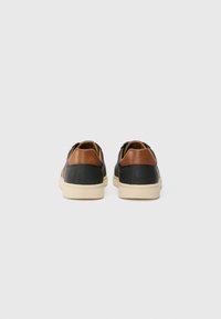 Adidași din piele neagră cu accente din piele maro, talpă din cauciuc crem și un design minimalist, cu texturi contrastante și linii curate.