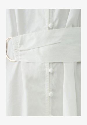 Biele šaty s textúrovanou látkou, širokým opaskom v páse, veľkým okrúhlym zlatým kovovým doplnkom a jemnými gombíkovými detailmi na prednej strane.