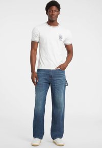 Witte katoenen T-shirt met grijze afwerking en een print op de borst, gecombineerd met blauwe denim jeans met een rechte pijp en lichte vervaging. Witte sneakers.