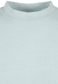 Chemise bleu clair à col rond montrant le col et le haut de la poitrine avec une texture douce en coton et des détails de couture fins.
