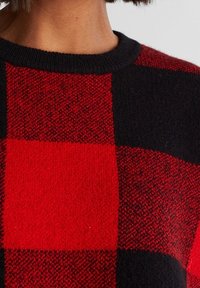 Suéter a cuadros rojo y negro con un diseño de tejido texturizado, que presenta un cuello redondo acanalado y un patrón de tablero de ajedrez en contraste.
