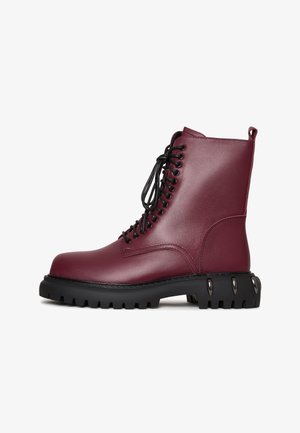 Bordeaux leren enkelboots met zwarte veters, een stevige zwarte rubberen zool en een ronde neus. Beschikt over een textuur zijpaneel en metalen accenten.