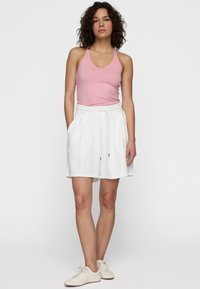 Top sin mangas de color rosa claro combinado con pantalones cortos deportivos blancos hasta las rodillas, con bolsillos laterales y cintura elástica. Zapatillas beige completan el conjunto.