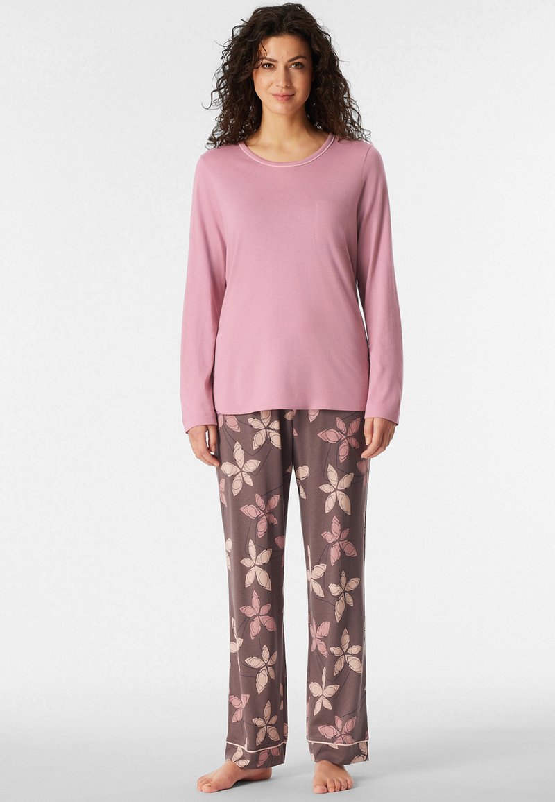 Top rosa chiaro a maniche lunghe con tasca, abbinato a pantaloni marrone scuro con un motivo floreale in rosa chiaro e crema.