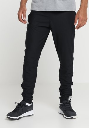 Sorte sports joggers med en slim fit, der har en hvid stribe langs siden, lavet af et glat stof, og parret med sorte sportsko.