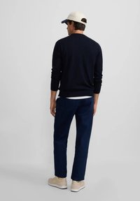 Suéter navy, vaqueros azules, zapatillas ligeras y una gorra beige. El suéter tiene un diseño ajustado y mangas largas, con una banda acanalada en el dobladillo.