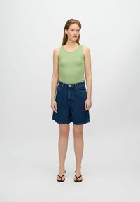 Débardeur côtelé vert avec encolure ronde associé à un short en denim foncé taille haute, présentant une coupe décontractée et des détails de couture.