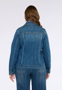 Geacă din denim cu dungi verticale, de culoare albastră, guler clasic, manșete cu nasturi și buzunare pe spate. Are talie ajustată și detalii cusute.