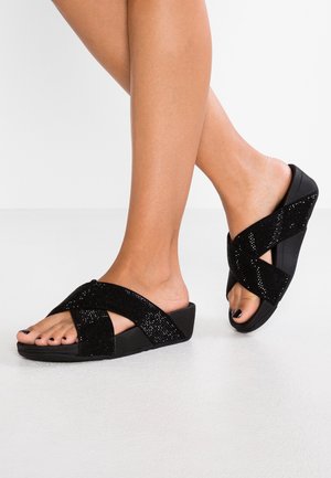 Schwarze Keil-Pantoletten mit überkreuzten Riemen und einer strukturierten, funkelnden Oberfläche. Die Sohle ist fest und leicht erhöht.