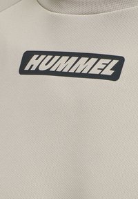 Långärmad, krämfärgad mesh-sporttop med en stor svart "HUMMEL"-logotyp på bröstet. Texturerat tyg med en figurnära design.