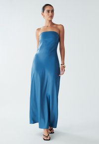 Obleka brez naramnic do tal iz gladkega modrega materiala, z oprijetim korpusom in letečo krilo. V kombinaciji s črnimi japonkami.