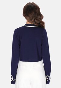 Námořnicky modrý zkrácený svetr s dlouhými rukávy, zdobený perlovými detaily na límci a manžetách. Hladký materiál s přiléhavým střihem.