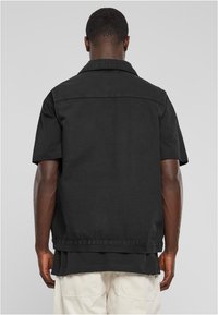 Camisa corta de manga negra con cuello, que presenta un diseño limpio en la parte posterior, confeccionada en denim con una textura suave.