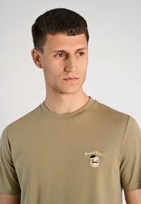 Koszulka w kolorze oliwkowej zieleni o dopasowanym fasonie, z małym haftowanym logo przedstawiającym kromkę tostu wraz z napisem "French Toast" w kontrastowych kolorach.