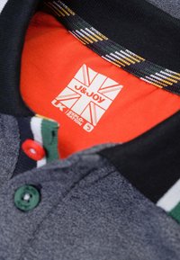 Grijze polo met een zwarte kraag met een veelkleurig gestreept patroon, groene en rode knopen, en een rode binnenlabel met het merkembleem.