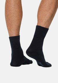 Sorte bomuldsankelsokker med ribbet manchet, vist på fødderne fra siden, med en glat tekstur og subtil logodetalje.