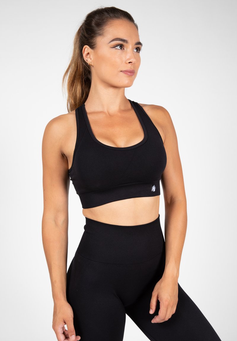 Zwarte atletische crop top met brede banden en geribbelde band. Gladde textuur en minimalistisch ontwerp, gecombineerd met hoge taille zwarte legging.