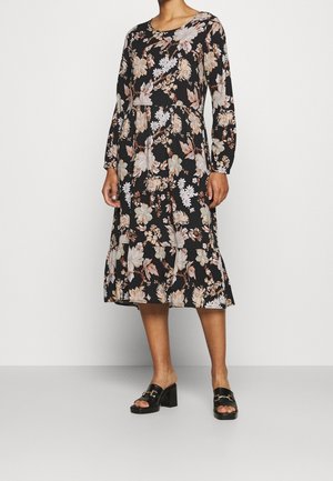Schwarzes, langärmeliges Blumenkleid mit beigen und weißen Mustern, geraffter Taille und ausgestellt geschnittenem Saum; kombiniert mit schwarzen Sandalen mit Blockabsatz.
