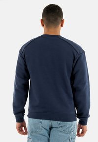 Felpa blu navy con polsini e orlo a costine, dotata di un classico collo rotondo e una texture di tessuto liscia. Cuciture visibili sulle cuciture delle spalle.