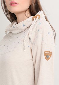 Krämbelagd hoodie med cowl-hals, prydd med färgglada segelbåtsmotiv, dragsnören och en logotypmärke på ärmen. Mjuk textur.