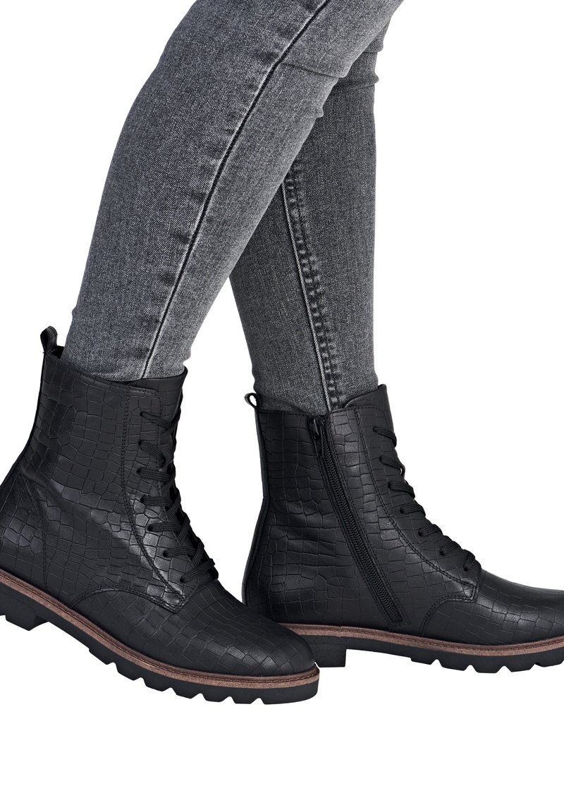 Black lace-up ankle boots with crocodile texture, a side zipper, rugged soles, and brown accents. Paired with gray slim-fit jeans.