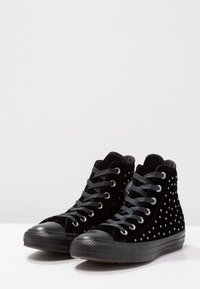 Svarta sammetshöga sneakers med vita prickar, grå snörningar och svarta gummitåhättor. Texturerat tyg och flexibel design.