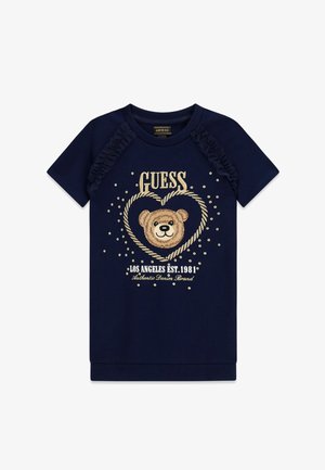 Camisa azul marino de manga corta con volantes en los hombros, dibujo de cara de oso de peluche dentro de un corazón, y texto "GUESS Los Angeles EST. 1981" en la parte delantera.