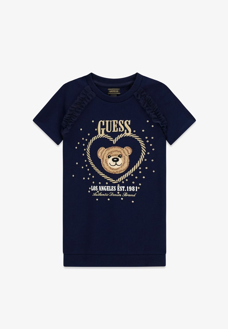 Chemise bleu marine à manches courtes avec épaules volantées, visage d'ours en peluche dans un graphisme en forme de cœur, et texte "GUESS Los Angeles EST. 1981" sur le devant.